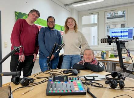 Vier Personen im Podcast-Studio mit Mikrofonen